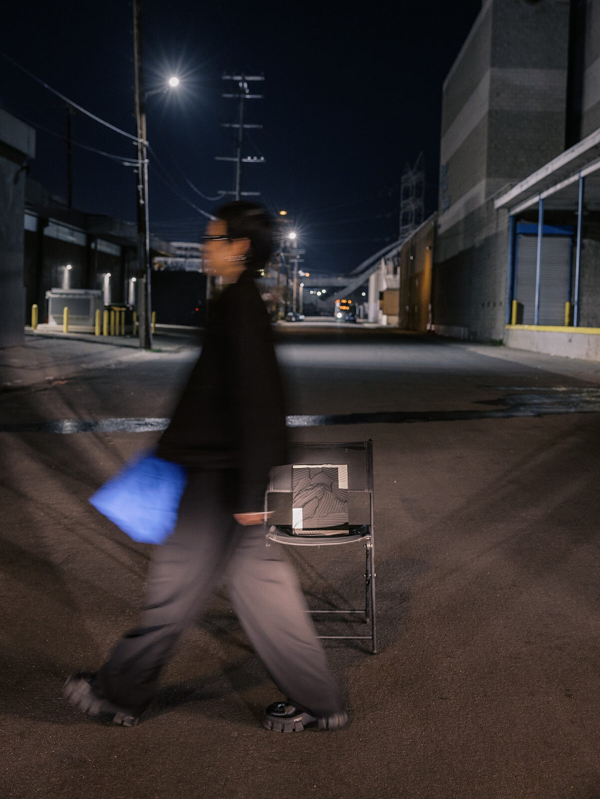 A crew member walks a wrapped painting past a folding chair on a night street during the film shoot