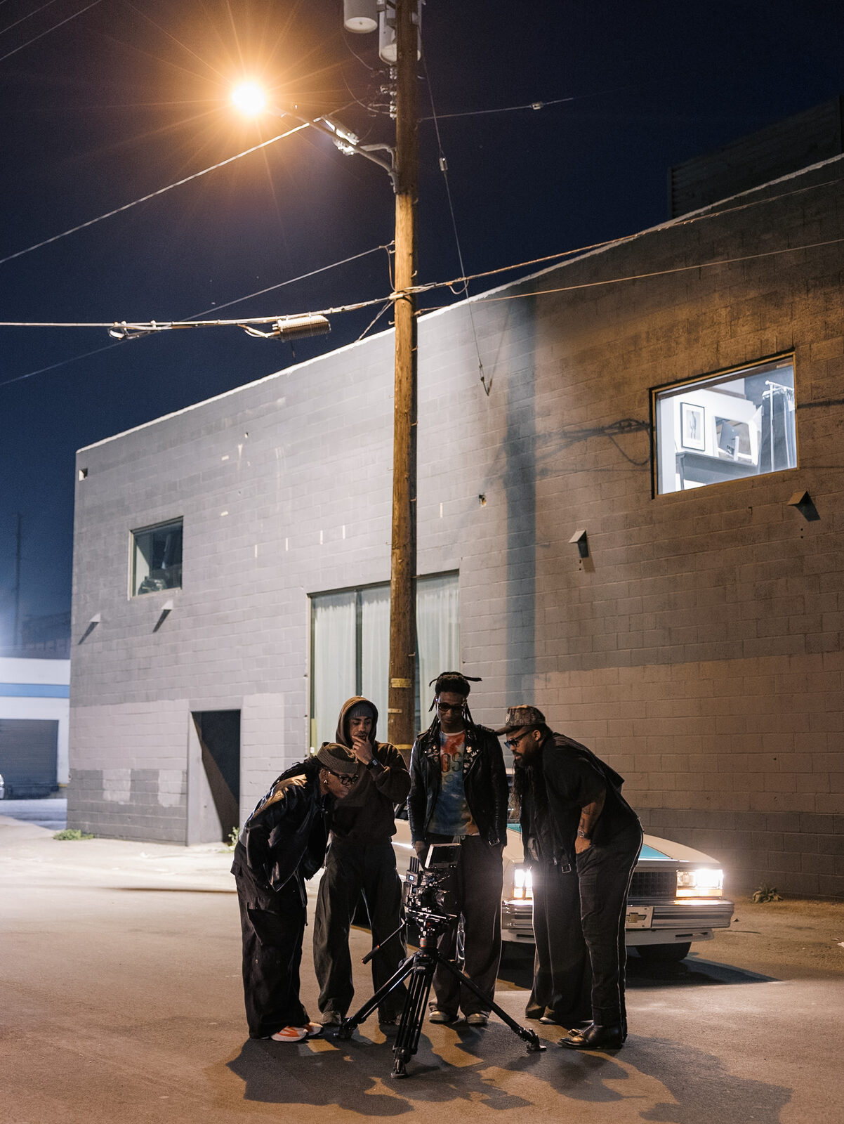 Four crew members review a shot on the camera monitor beside a parked car at night