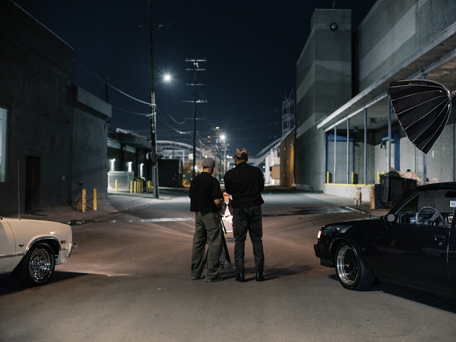 Two crew members set a camera and umbrella light at the end of a night street