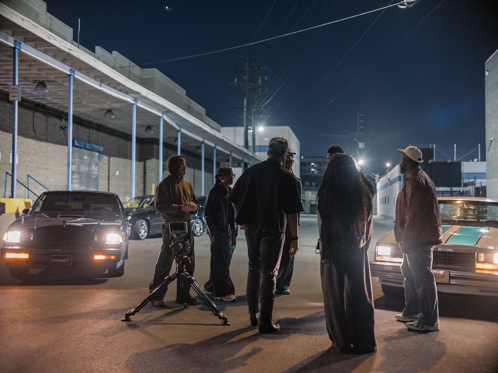 The crew gathers on a night street between two vintage cars during the shoot